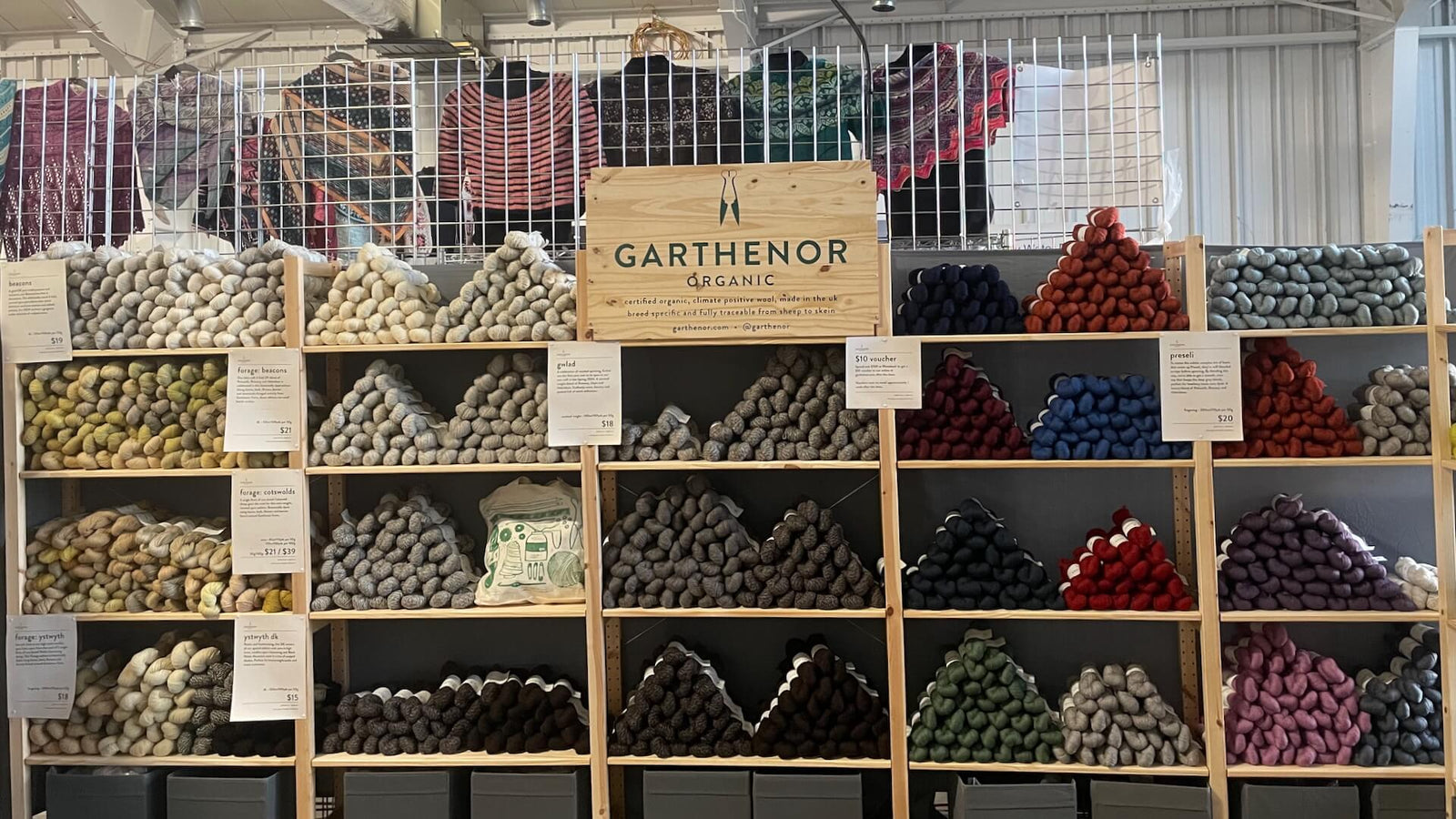 Garthenor Organic booth at Flock Fiber Festival with neatly stacked yarn pyramids and hanging knitted samples in background.