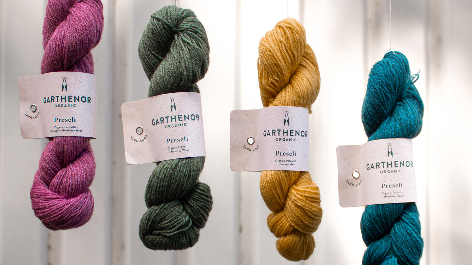 Four skeins of Garthenor Preseli fingering-weight yarn in bright pink, green, gold, and teal, used in Prado de Lana sock kits.