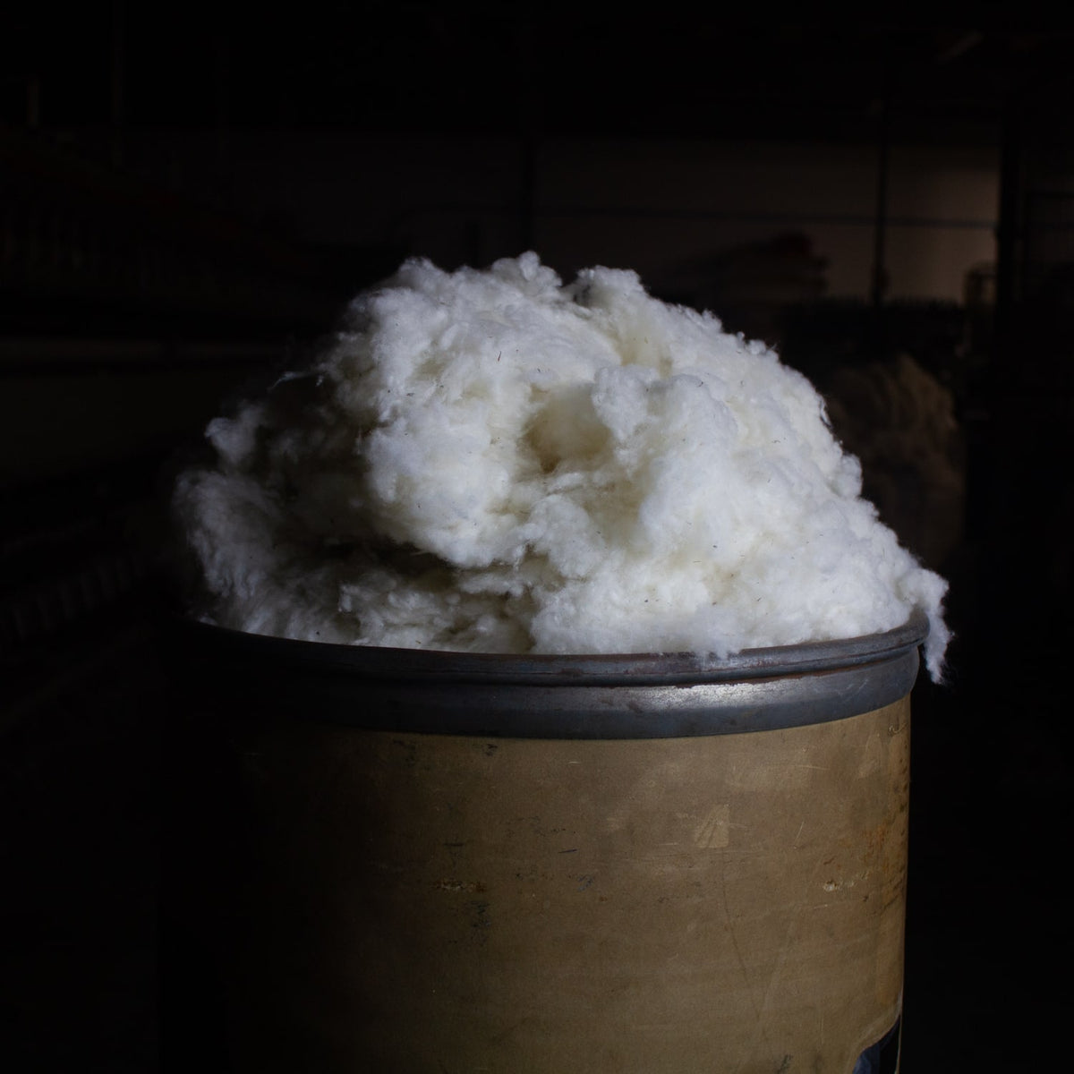 A sliver can is pictured overflowing with wool noil in natural white, used as organic wool stuffing
